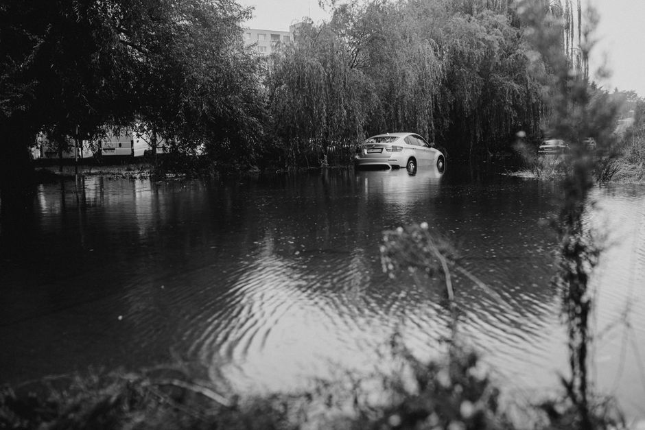 Two individuals are working in a flooded outdoor area, utilizing a large orange flood rescue truck equipped with various hoses, tools, and equipment for emergency flood cleanup. One person stands in t